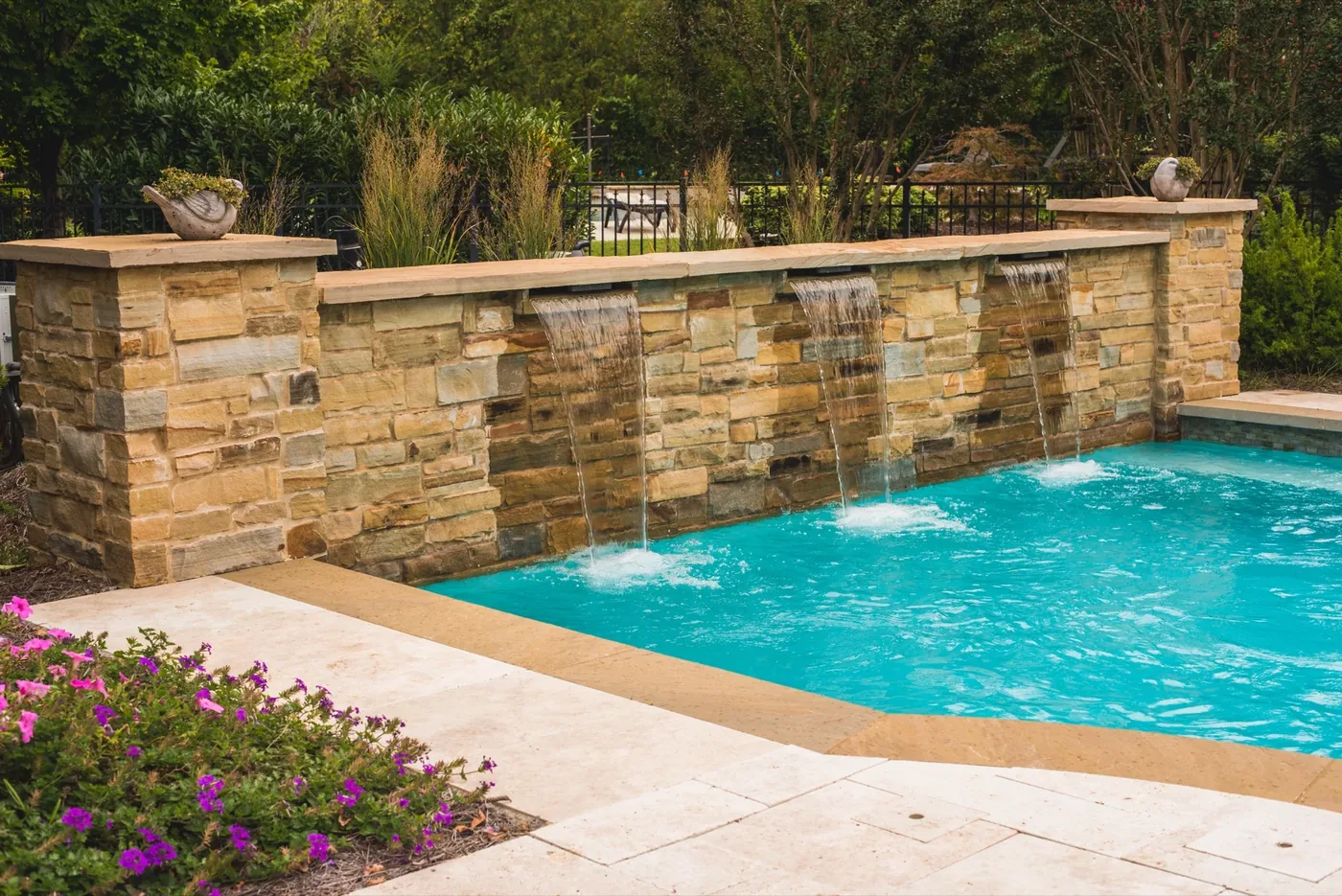 Stone waterfall wall with sheer descent waterfalls into pool at Francis Residence, built by Waterscapes