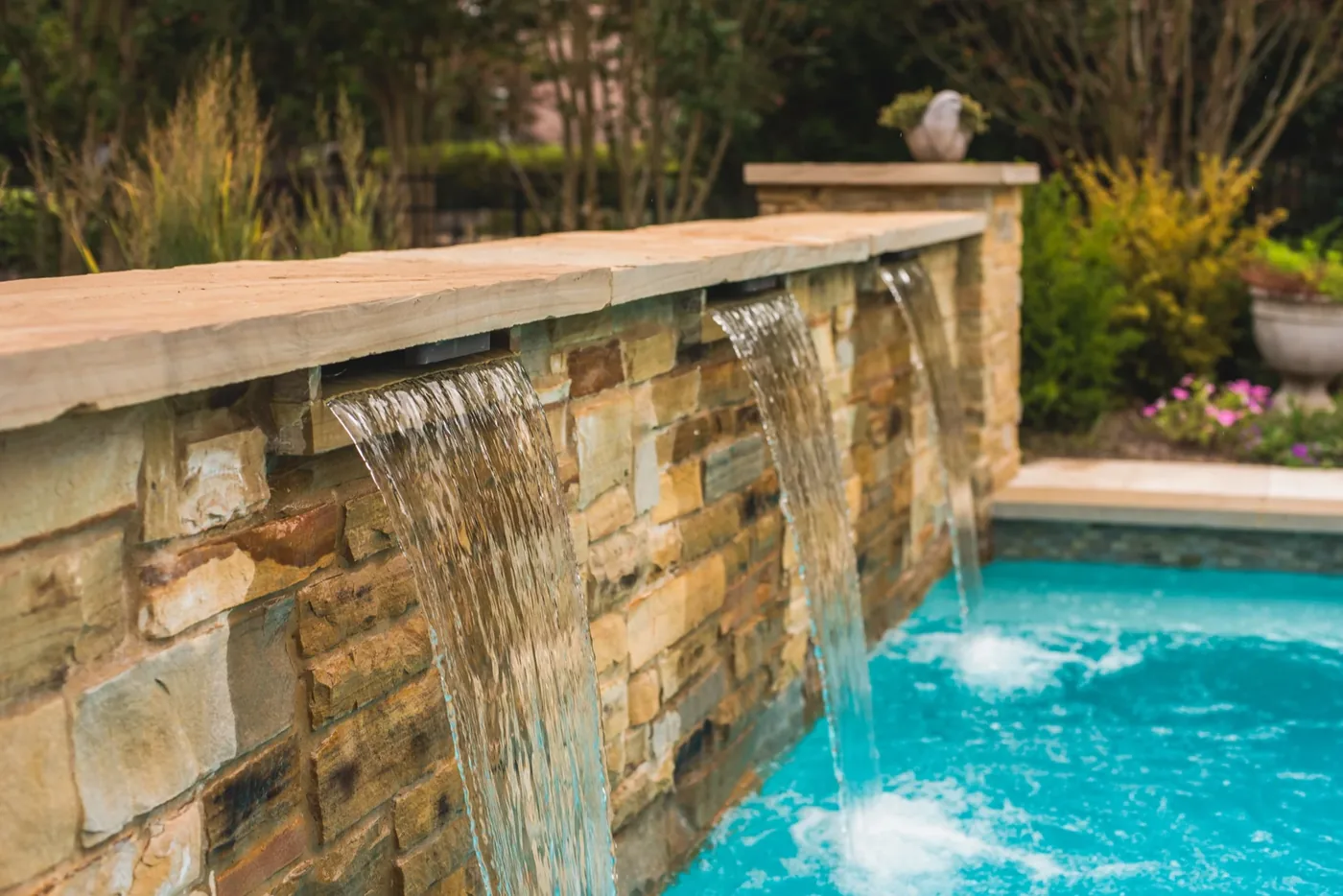 Close-up of sheer descent waterfalls cascading over natural stone wall into pool at Francis Residence