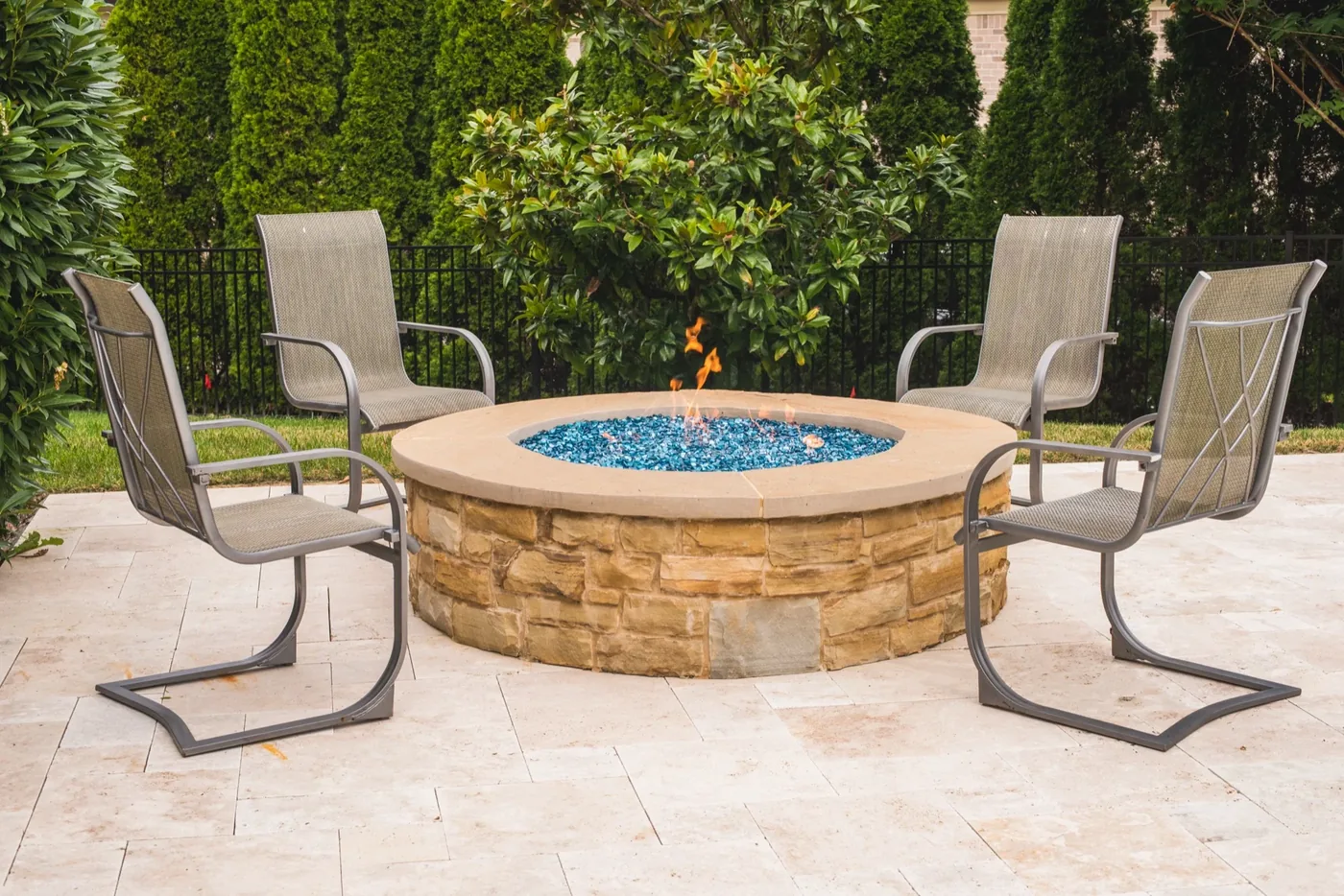 Round built-in stone fire pit with seating on travertine patio at Francis Residence