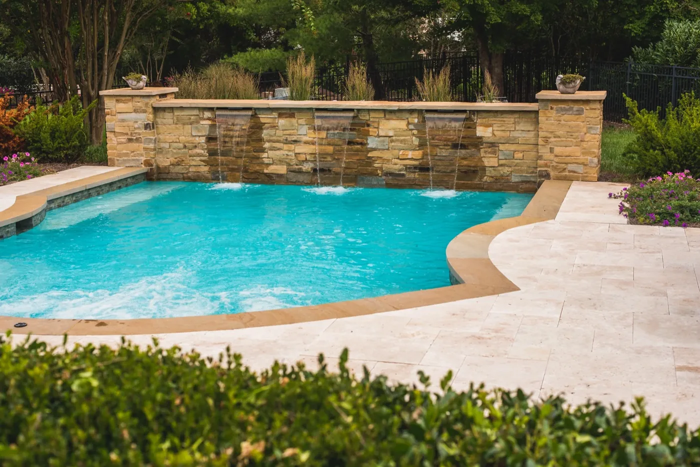 Full pool view with stone waterfall wall and travertine deck at Francis Residence