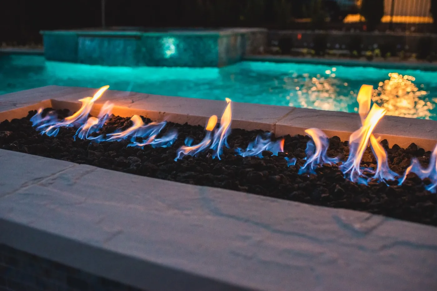 Built-in linear fire feature with pool and elevated spa glowing behind it at Tarkington Residence