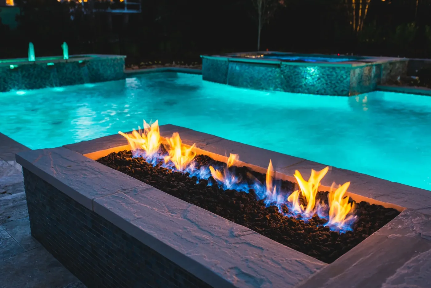 Linear fire pit with spa, pool, and fountain jets in background — full fire and water integration at Tarkington Residence