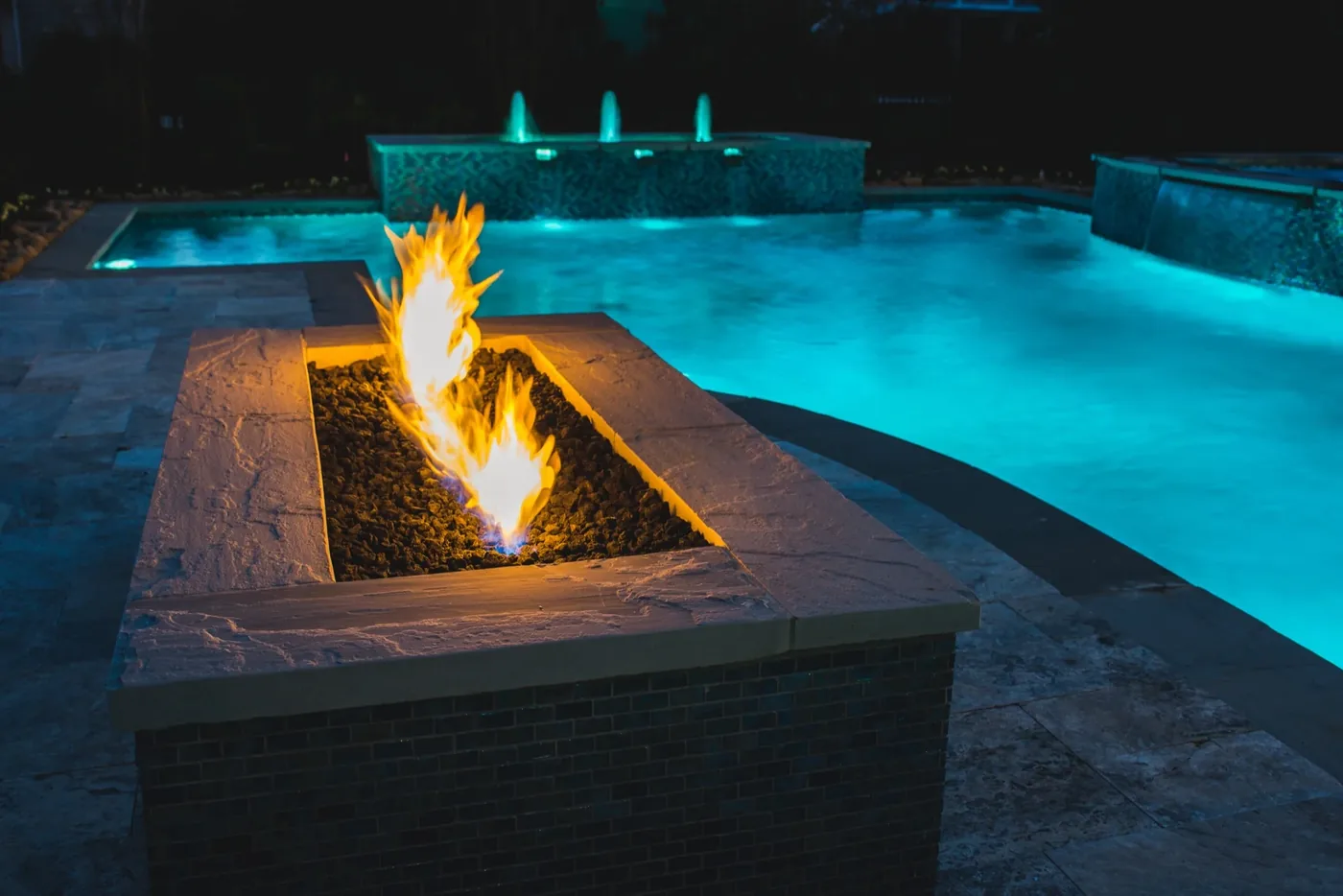 Fire feature in foreground with fountain jets and sheer descent water feature behind at Tarkington Residence