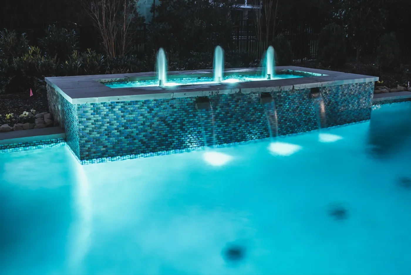 Elevated glass tile spa with illuminated fountain jets and sheer descent spillover at Tarkington Residence